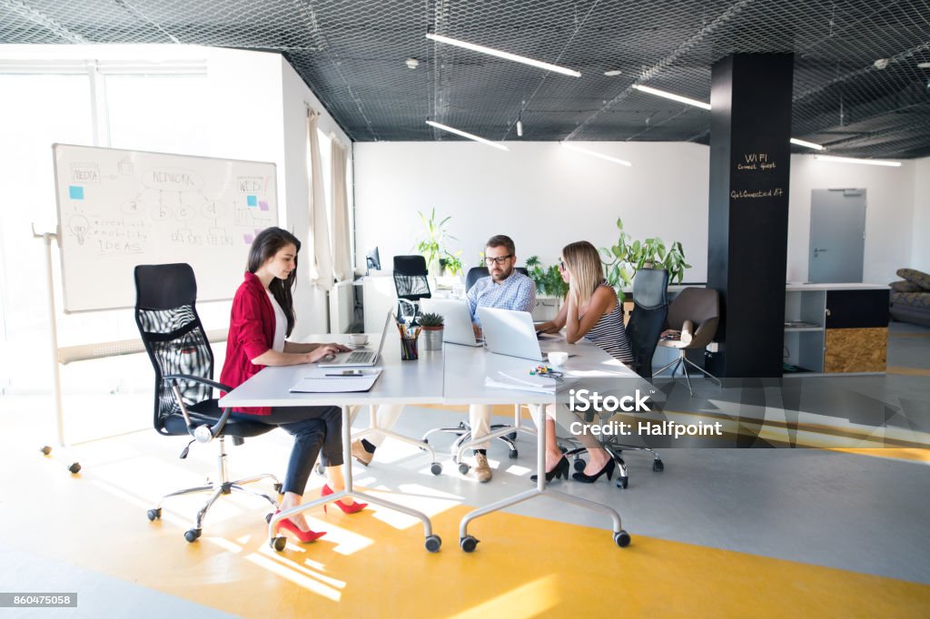 Three business people in the office talking together. Three business people in the workplace. Two women and man sitting in the office working together. Office Stock Photo