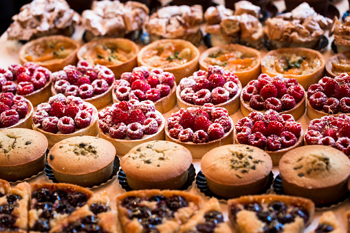 Close up horizontal color image depicting a selection of freshly baked delicious cakes and cupcakes for sale at Borough Market in London, one of the oldest and most popular food markets in the world. Room for copy space.