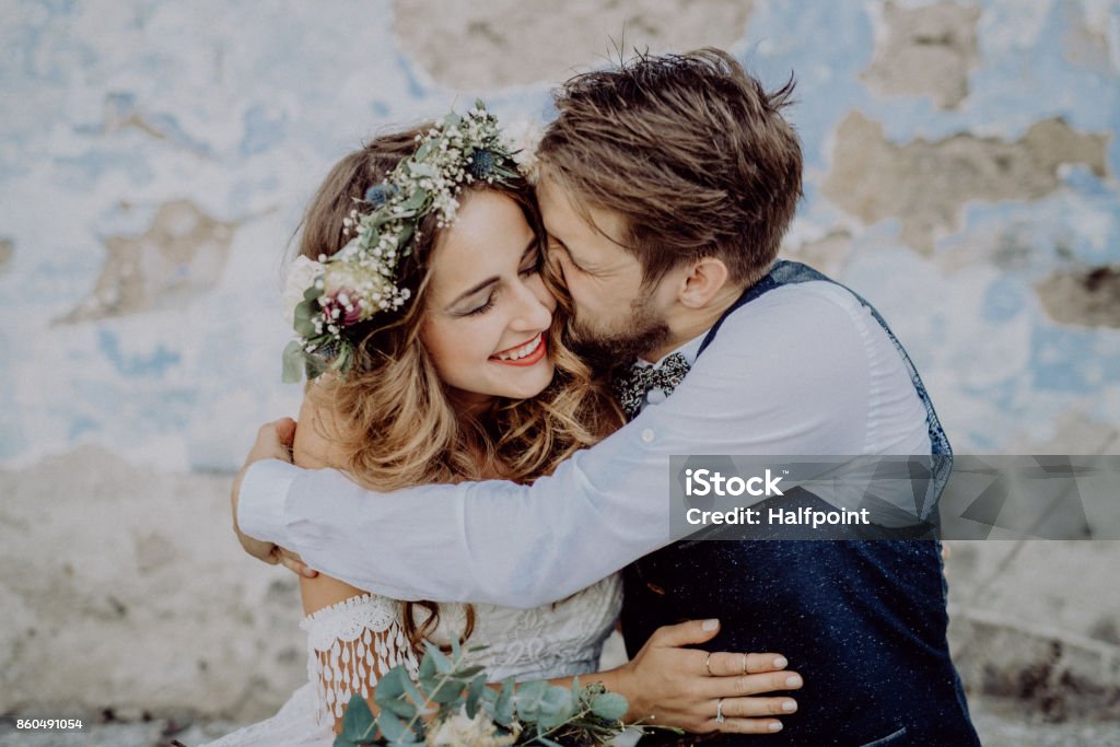 Beautiful bride and groom in front of old shabby house. Beautiful young bride and groom outside in front of an old shabby house kissing. Wedding Stock Photo