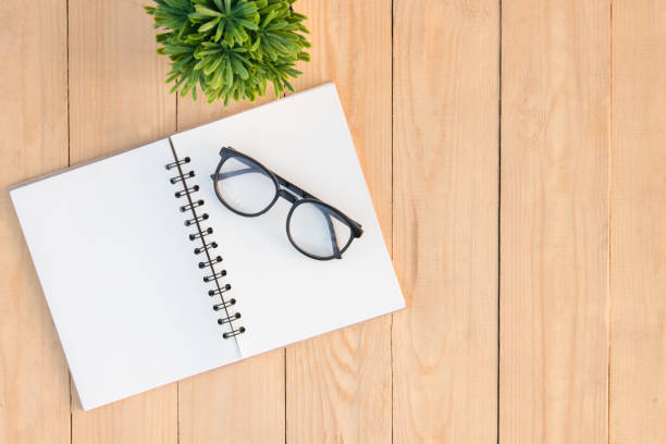 istock Eyeglasses on blank book and small tree on wooden table. copy space 860492688