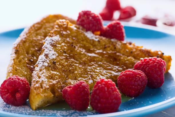 Two french toasts on a plate, with powdered sugar,raspberries and honey