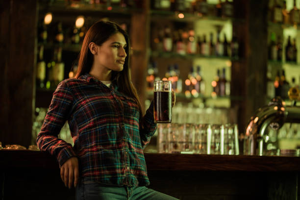 Young woman holding pint of beer and looking away while spending night out in a bar.