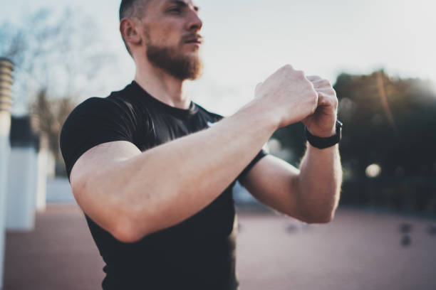 istock Workout lifestyle concept.Young man stretching his arm muscles before training.Muscular athlete exercising outside in sunny park. Blurred background. 860499194