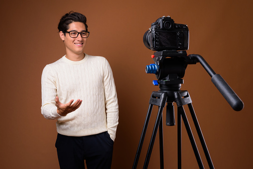 Studio shot of young multi-ethnic handsome man vlogging against colored background horizontal shot