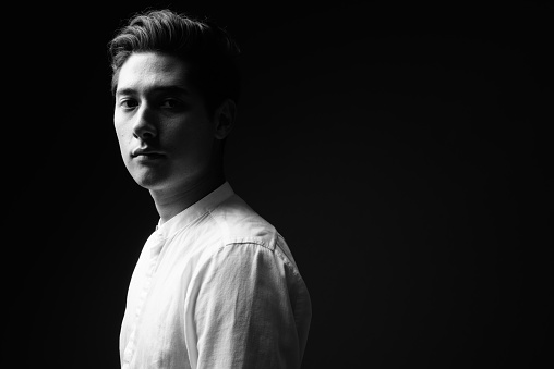 Studio shot of young multi-ethnic handsome man against black background in black and white horizontal shot