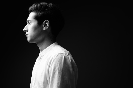 Studio shot of young multi-ethnic handsome man against black background in black and white horizontal shot
