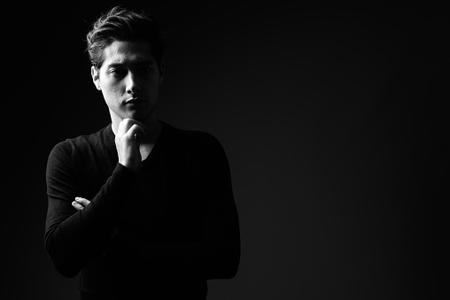 Studio shot of young multi-ethnic handsome man wearing black sweater against black background in black and white horizontal shot