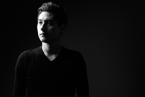 Studio shot of young multi-ethnic handsome man wearing black sweater against black background in black and white horizontal shot