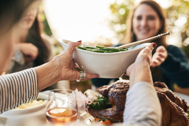 Please pass the beans Shot of a unrecognizable woman passing on a plate of green beans to a cheerful woman at lunchtime over a table typical average stock pictures, royalty-free photos & images