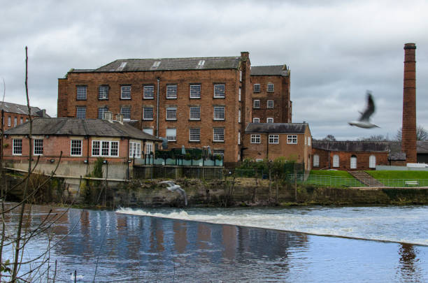 The Boar's Head Cotton Mills in Derby, Derbyshire, England, UK The old factory building stands in Darley Abbey. The river Derwent is visable in the foreground. derby city stock pictures, royalty-free photos & images