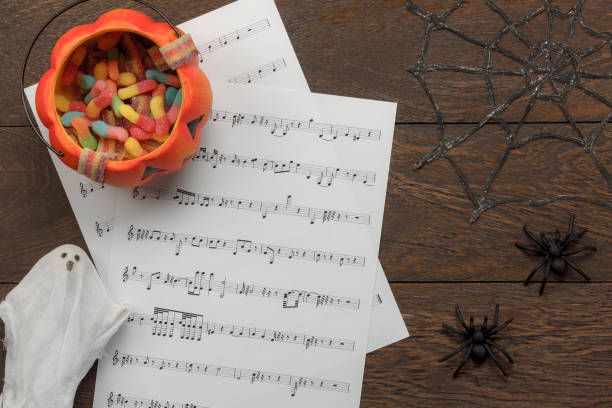 Above view of  Happy Halloween Festival and music note sheet background concept.Trick or treat bowl and decorations items on modern brown table.Mix variety object idea for season with copy space. stock photo