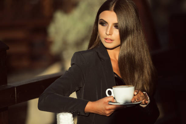 Fashion business woman is wearing black official clothes drinking coffee outdoors stock photo