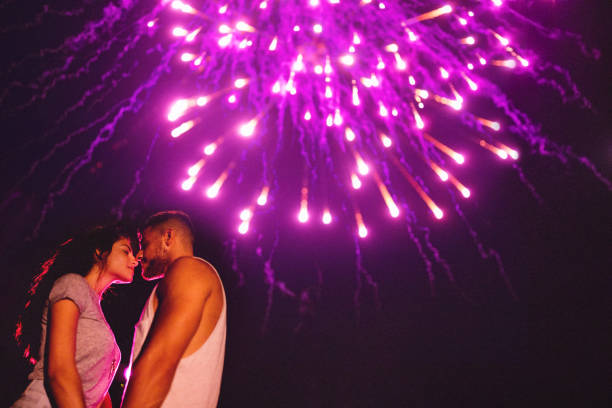 istock Young romantic couple kissing below fireworks display in the sky 860566282