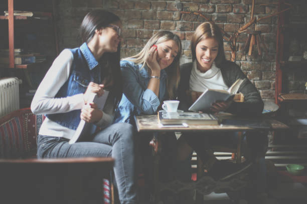 istock Three young girls student sitting in cafe and reading book. 860571018