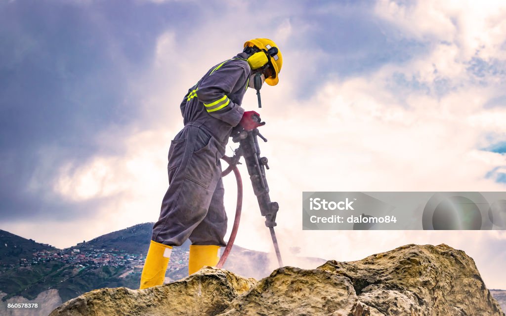 Worker on top of a rock Worker with helmet and protective suit using a drilling machine on top of a large rock Mining - Natural Resources Stock Photo