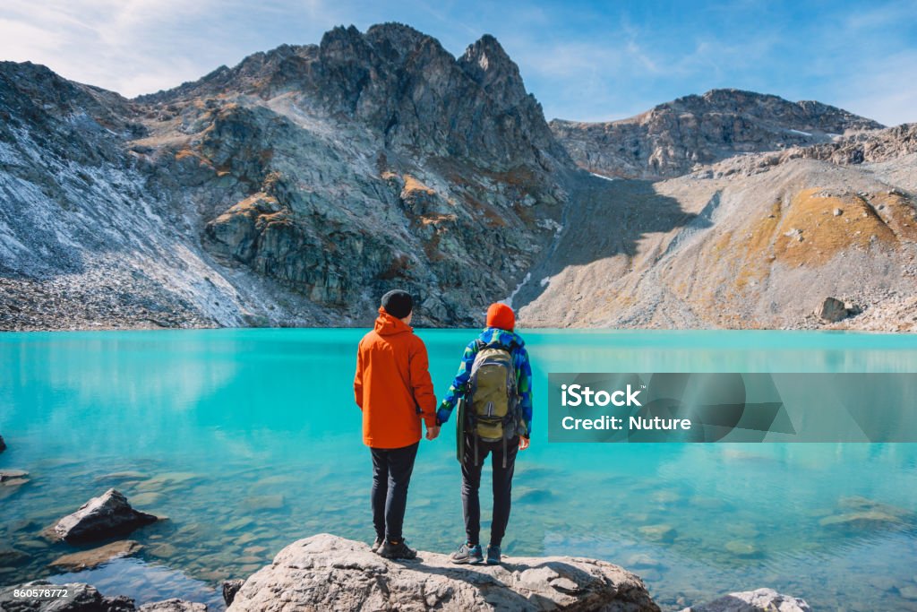 Pareja de turistas se ve en el lago. Luna de miel en los Alpes. Hermoso lago de color turquesa en las montañas. - Foto de stock de Parejas libre de derechos