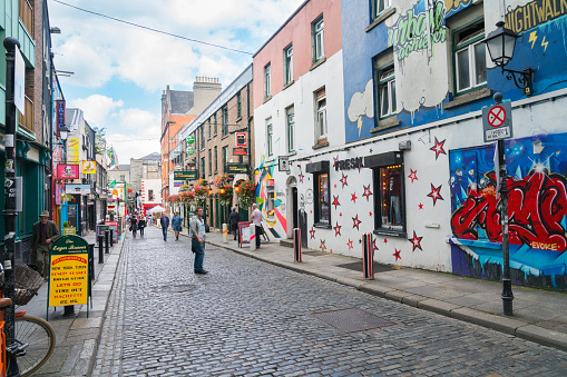 DUBLIN, IRELAND - AUGUST 10, 2017; Few people leisurely browsing and walking  along narrow quaint cobbled street in Temple Bar area with shop signage  and street art on both sides
