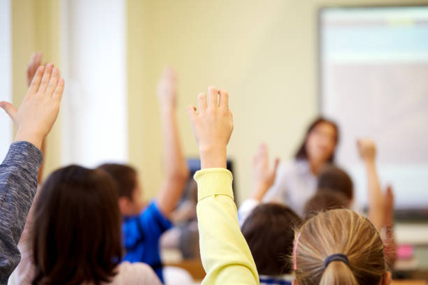 istock group of school kids raising hands in classroom 860595276