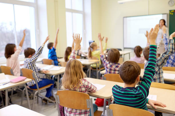 istock group of school kids raising hands in classroom 860597978