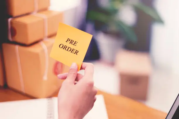 "Pre-Order" text on post it paper in woman hand at post office with many boxes, Online shopping and Marketing concept idea. Split and cross processing tone pinterest and instragram like process.