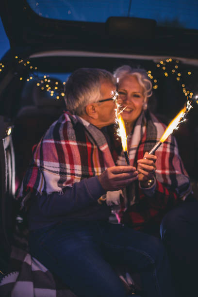 istock Senior couple sit in open car trunk and hold spark sticks in their hands 860606068