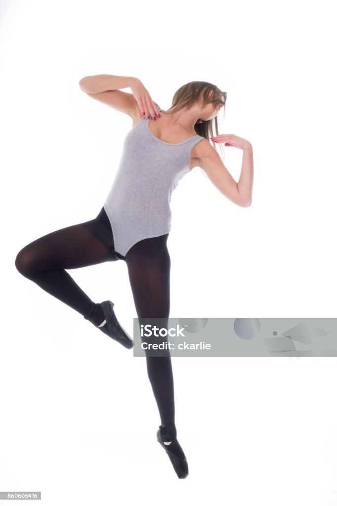 dançarina bonita jovem com longos cabelos negros vestindo camisa cinza e collants saltando sobre um fundo de luz studio branco - Foto de stock de Adulto royalty-free