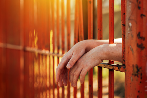 Female hands behind prison yard bars, incarcerated captivated person in jail