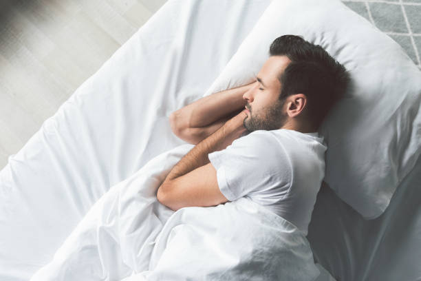 Cute young man sleeping on bed Top view of calm guy napping in his bedroom with enjoyment. Copy space peace sign gesture photos stock pictures, royalty-free photos & images