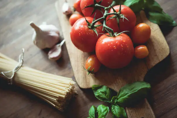 Photo of Spaghetti, garlic, basil and tomatoes on a cutting board