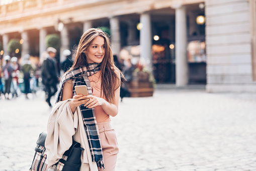 Fashionable woman holding phone and walking on the street