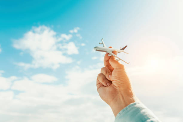 mano que sostiene el modelo de avión delante de fondo de cielo azul nublado. concepto de transporte de aire. - foto de stock