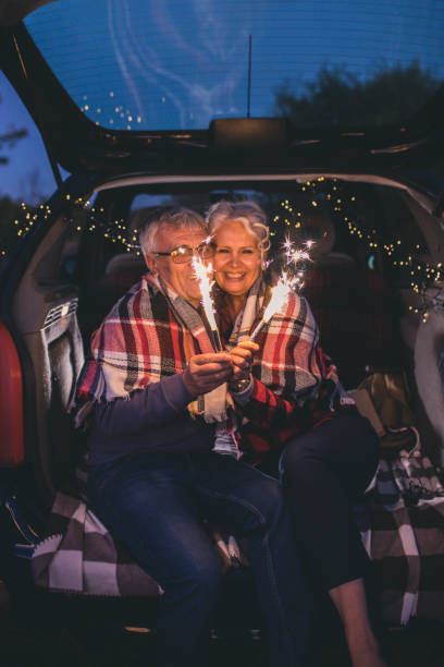 istock Senior couple sit in open car trunk and hold spark sticks in their hands 860624732