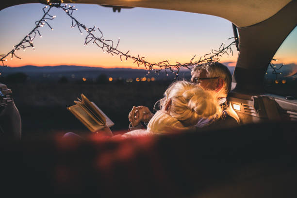 Senior couple sit in open car trunk and reading a book stock photo