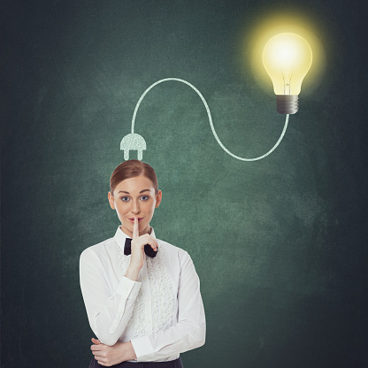 Portrait of businesswoman making silent gesture with light bulb plugged on her head