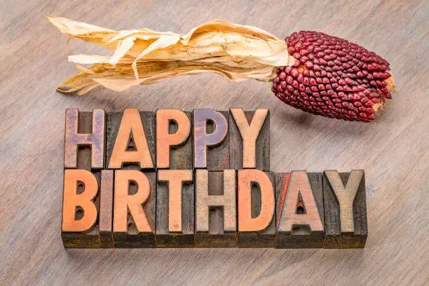 Happy Birthday greeting card in vintage letterpress wood type against grained wood with a decorative strawberry corn