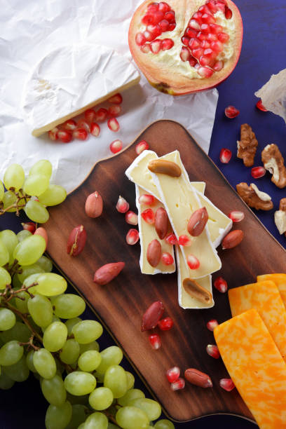 istock Camembert cheese, orange hard cheese, green grapes, peanuts, walnut and pomegranate seeds on a wooden board on a dark blue background 860646172