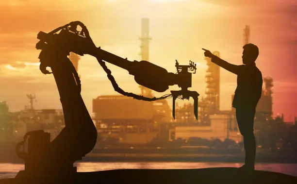 Photo of Industry 4.0 technology , artificial intelligence trend concept. Silhouette of business man point finger forward to heavy automation robot arm machine. Vivid sunset sky and smart factory background.