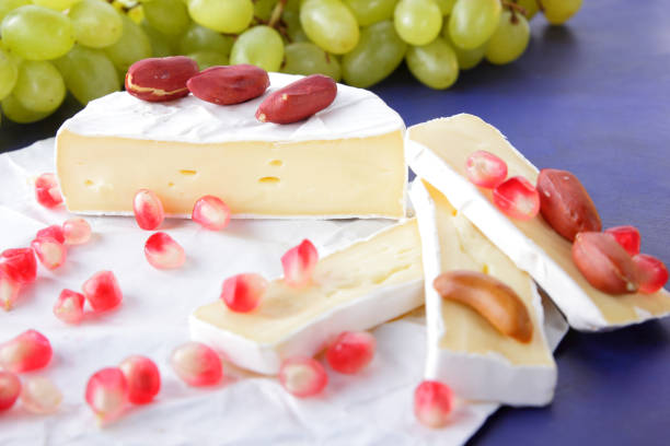 camembert käse, in scheiben geschnittenen käse, weichkäse mit schimmel, grüne trauben, erdnüsse und granatapfelkernen auf dunkelblauem hintergrund - american beech stock-fotos und bilder