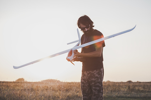 Man preparing to launch RC glider. Man with long dark beard on the meadow with RC glider in his hand in the Sun backlight. Horizontal image