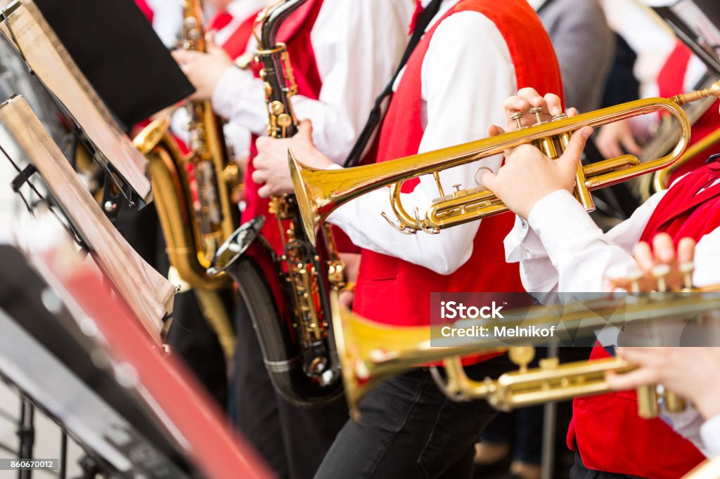 musical instrument, brass band and orchestra concept - closeup ensemble of musicians playing on trumpets and saxophones in red concert costumes, male hands with shiny equipment, selective focus Jazz Festival Stock Photo