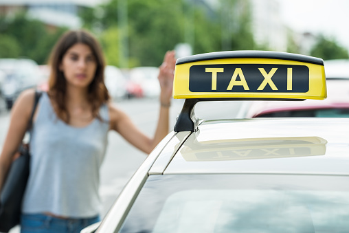 Young Woman Raising Arm To Hail Taxi On Street