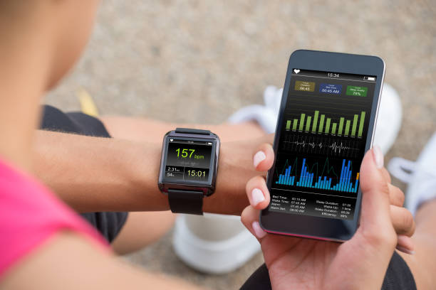Running Female With Mobile Phone Connected To A Smart Watch Female Runner Looking At Her Mobile And Smart Watch Heart Rate Monitor wristwatch photos stock pictures, royalty-free photos & images