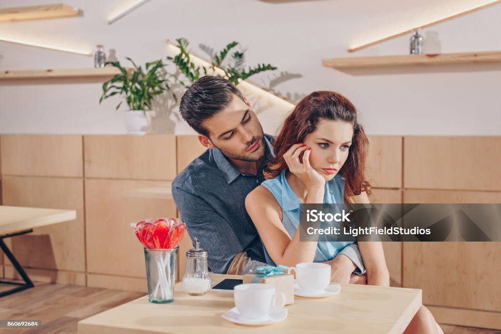 couple on romantic date man hugging upset girlfriend while having romantic date in coffee shop Couple - Relationship Stock Photo