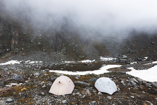 Ð¡amping with tents high in the mountains in winter. Fog, snow and cold weather. Mountain range and rocks on background