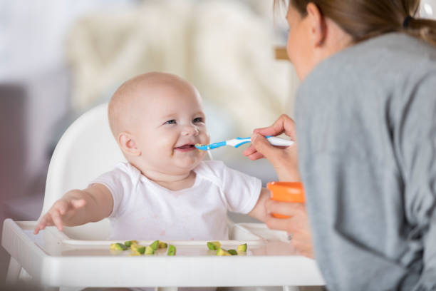 Adorable baby in high chair laughs while being spoon fed An adorable baby in a high chair laughs at her mother as she spoon feeds her.  She pretends the spoon is a moving train using sound effects. infant feeding stock pictures, royalty-free photos & images