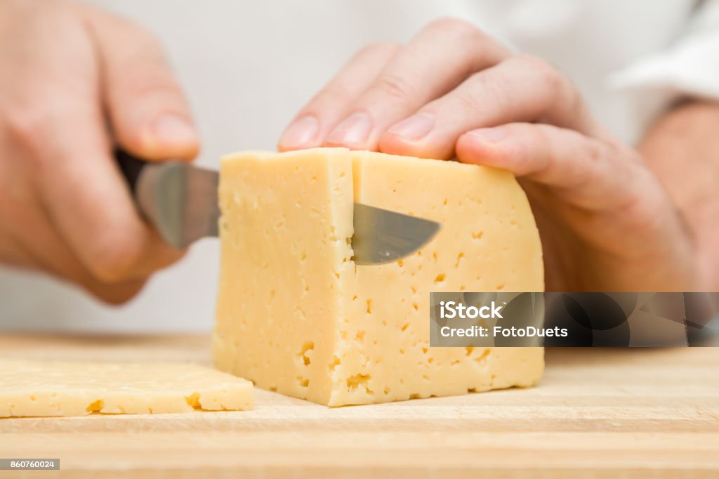 Chef's hands with knife cutting a cheese on the wooden board for sandwich, italian pizza or snack in the kitchen. Preparation for cooking. Healthy eating and lifestyle. Food concept. Cheese Stock Photo