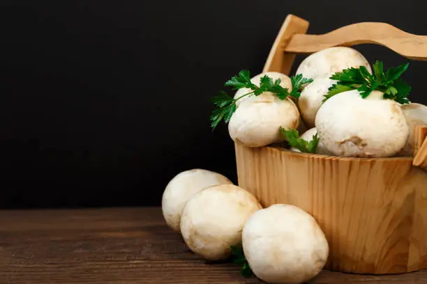 Fresh mushrooms to a wooden basket on a black background.