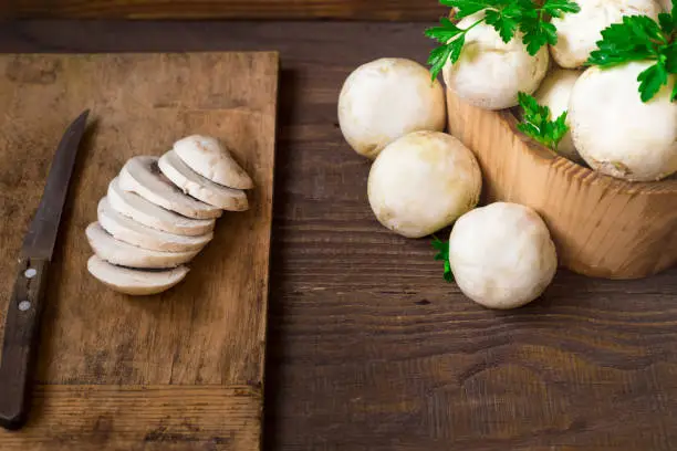 Fresh mushrooms in a wooden basket and on a wooden board lie cut.