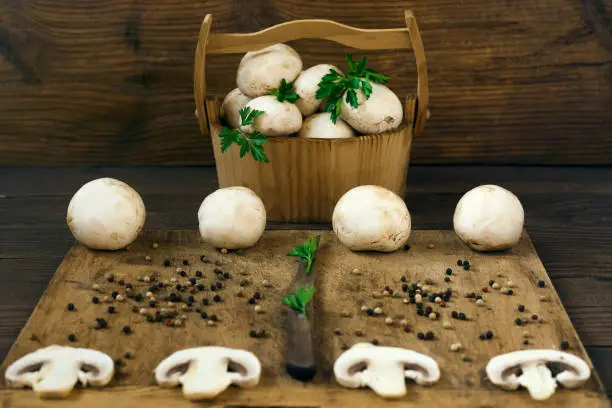 Fresh champignons in a wooden basket and cut on a chopping board.