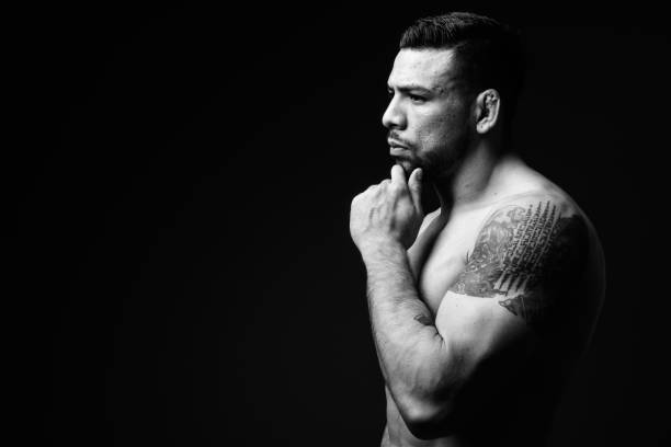 studio shot of young muscular hispanic man shirtless against black background - stubble men tattoo sensuality imagens e fotografias de stock